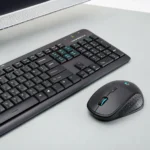 Black keyboard with Cyrillic and English characters next to a wireless mouse on a light gray desk.
