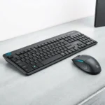 Black keyboard and matching mouse set on a gray desktop surface. The keyboard features a compact layout, and the mouse has ergonomic design elements.