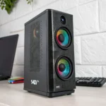 Black computer tower featuring two RGB cooling fans on a desk, surrounded by a laptop and keyboard in a well-lit room.