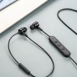 Black wired earbuds featuring an inline control panel with three buttons, placed on a light blue surface near the edge of a device.
