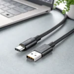 Close-up of a USB-C cable with braided design placed near a laptop on a gray desk.